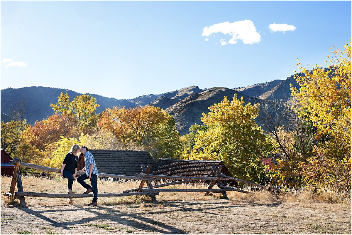 couple sitting on fence with trees and mountains, clear creek history park, golden colorado engagement session, autumn engagement session, l elizabeth events, colorado engagement photography, mountain engagement photographer