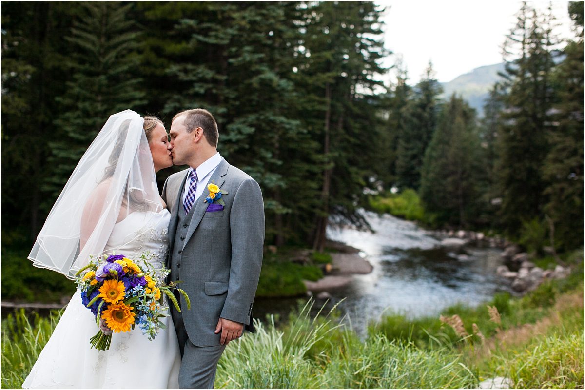 bride and groom portrait in front of river, purple and yellow floral, bridal bouquet, boutonniere, checkered tie, gray suit, donavan pavilion vail, colorado wedding photography, mountain wedding photographer