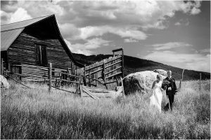 bride and groom portraits, holding hands walking, tall grass, mountain backdrop, old wood barn, steamboat springs, mountain wedding photographer, colorado wedding photography, black and white image, kissing