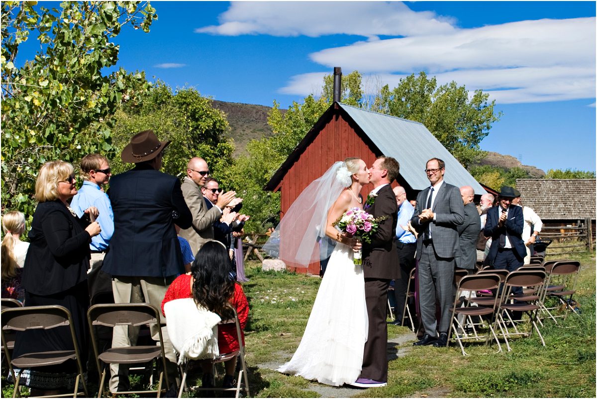 bride and groom kissing, recessional,wedding guests, outdoor ceremony in front of rustic red barn at clear creek history park, golden colorado, wedding photographer, colorado wedding planner